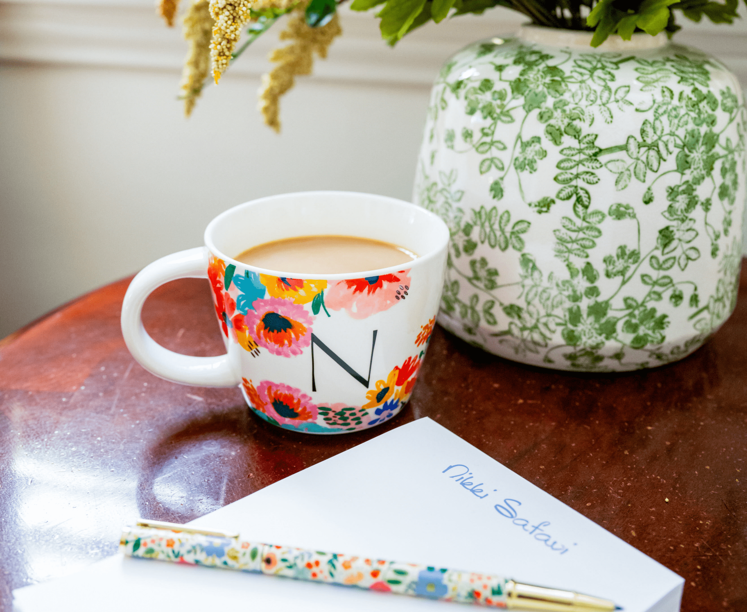 Coffee mug, floral pen and Nikki Safavi notepad on a desk